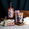 Apricot Vetiver hand care products including a bottle, tube, and soap on a wooden stand with flowers and a dark background.