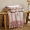 Beechwood Throw Camellia Stack of pink and white striped blankets on a wooden bench with a vase of flowers in the background.