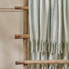 Beechwood Throw Moorland Green Striped blanket draped over a wooden ladder against a neutral background