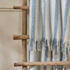 Beechwood Throw Sky Blue Striped blanket draped over a wooden ladder against a neutral background