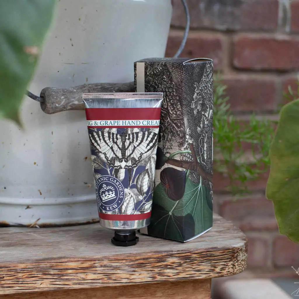 Hand cream tube with decorative packaging on a wooden surface with plants and a brick wall in the background
