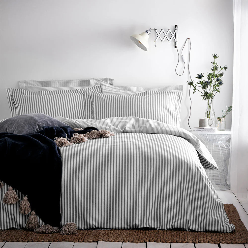 Bed with striped bedding in a bedroom setting with a lamp and plant.