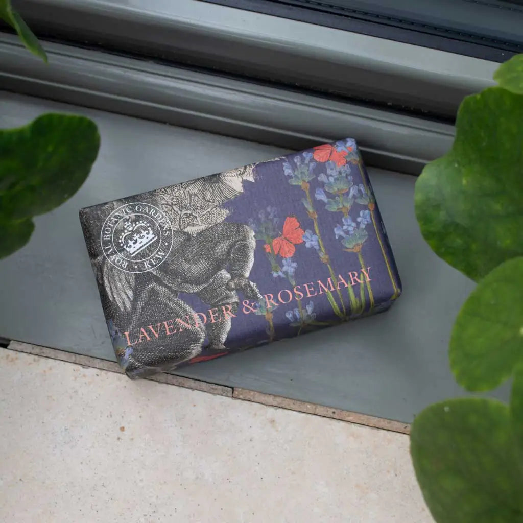 Bar of soap with floral design and text on a metallic surface, surrounded by green leaves.