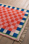 Checkered rug with red, blue, and pink squares on a wooden floor