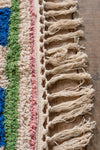 Close-up of a textured fabric with fringes and colorful stripes on a wooden surface.