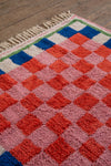 Colorful checkered rug with red, blue, and pink squares on a wooden floor.