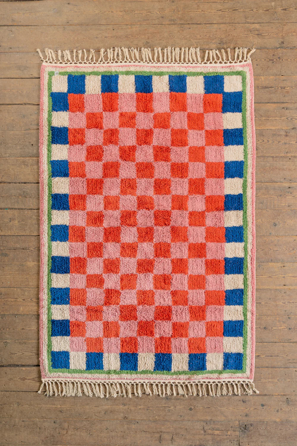 Checkered rug with red, blue, and pink squares on a wooden floor
