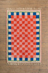 Checkered rug with red, blue, and pink squares on a wooden floor