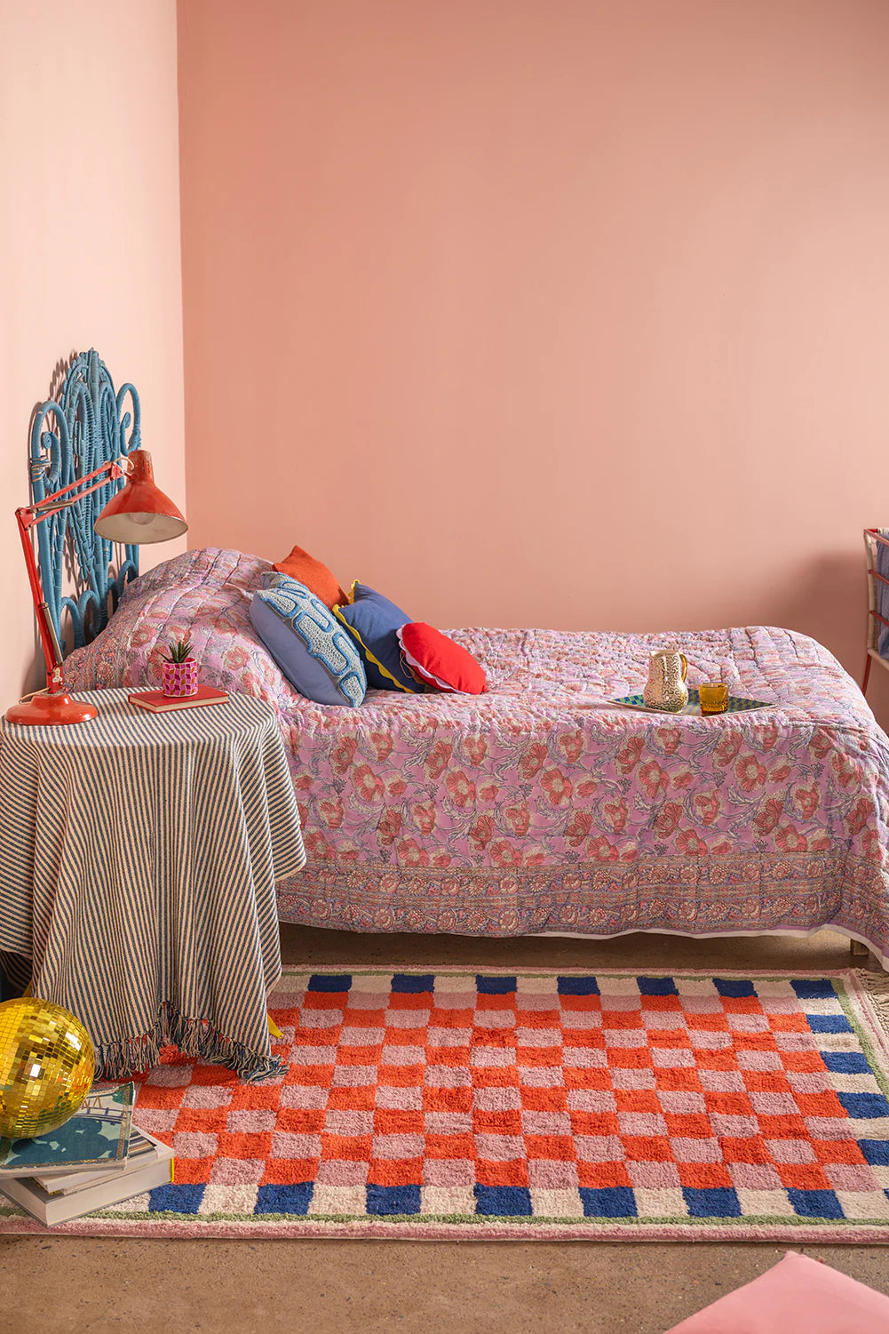 Bedroom with floral bedspread, colorful rug, and decorative pillows.