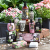 Collection of Magnolia & Pearl products including bottles, boxes, and soap on a wooden surface with flowers in the background.