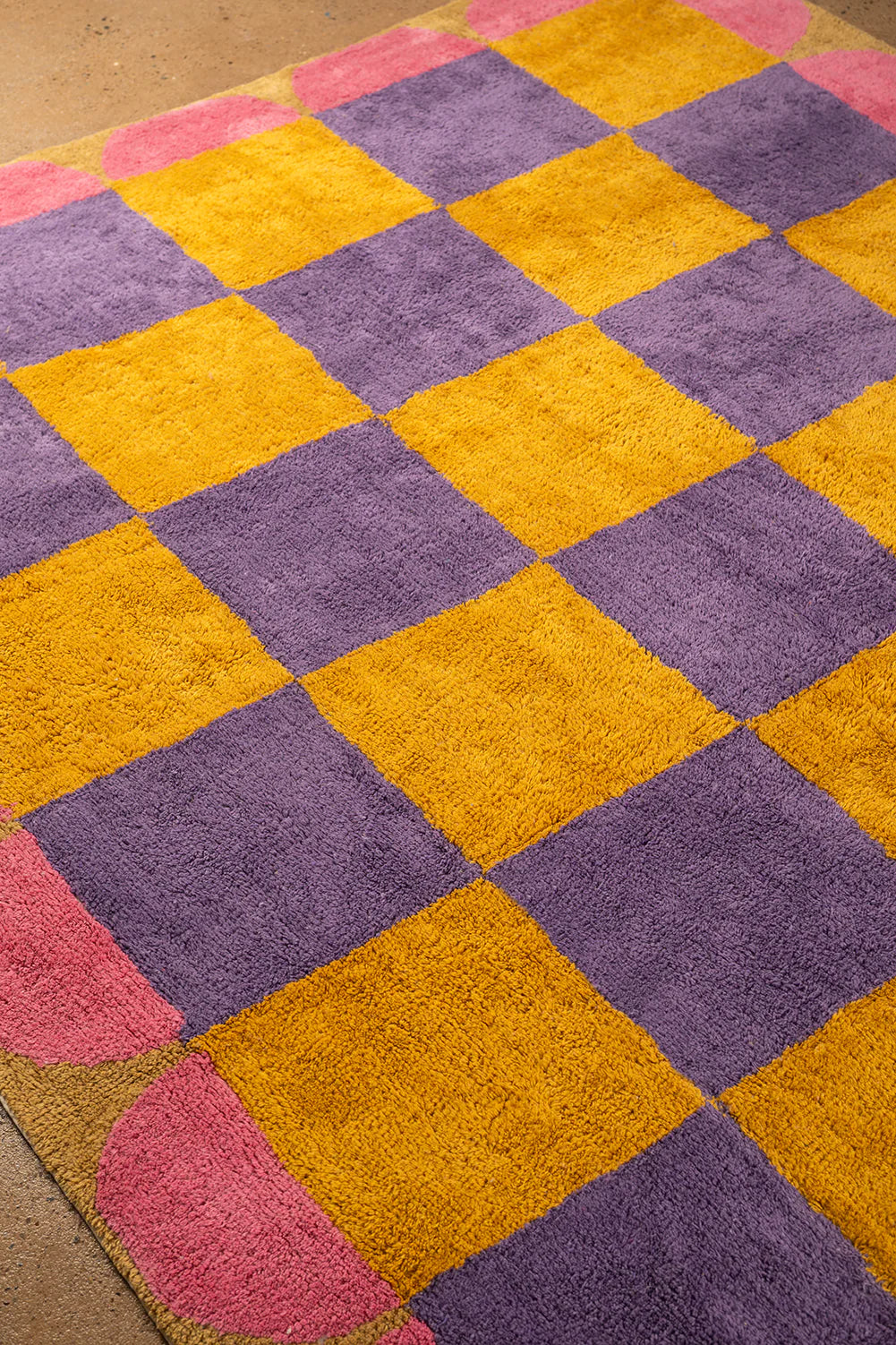 Checkered rug with purple and yellow squares on a wooden floor.