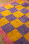 Checkered rug with purple and yellow squares on a wooden floor.