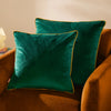 Two green velvet pillows on a brown armchair with a warm light in the background.