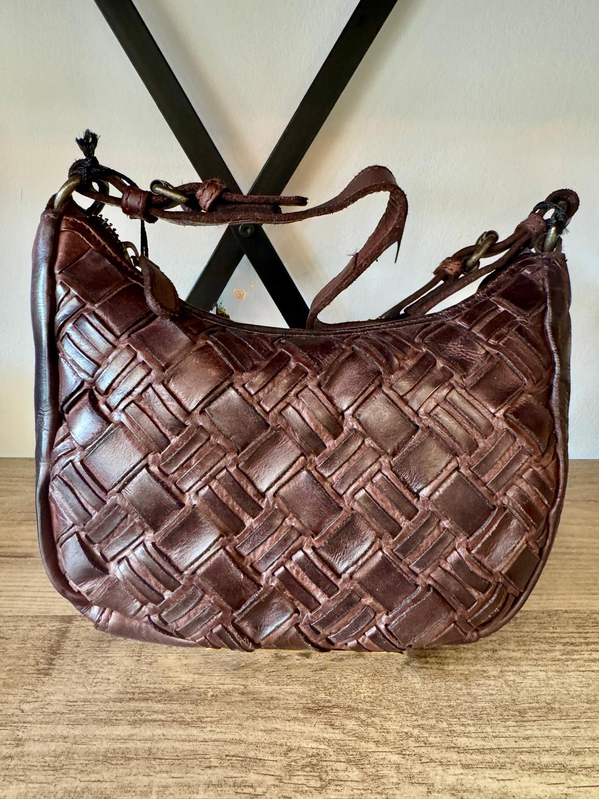 Brown woven handbag on a wooden surface with a neutral background