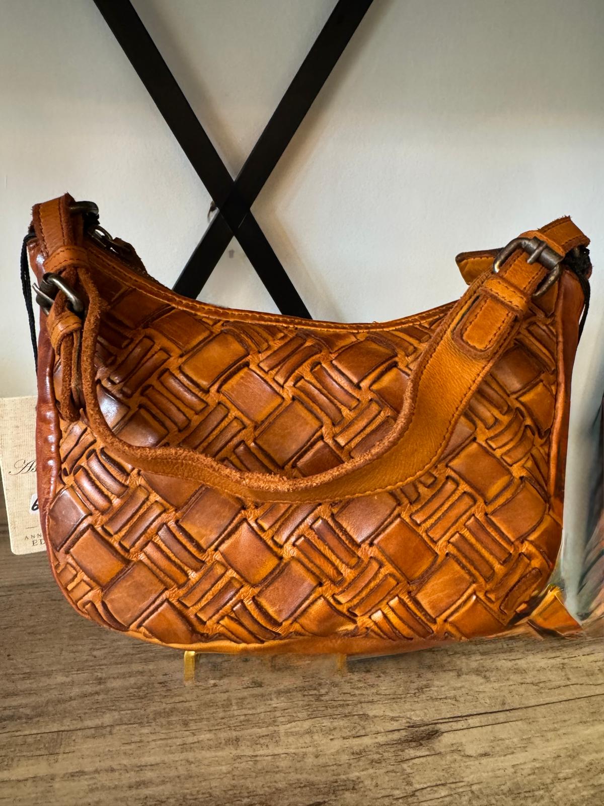 Brown woven handbag on a wooden surface with a white wall background