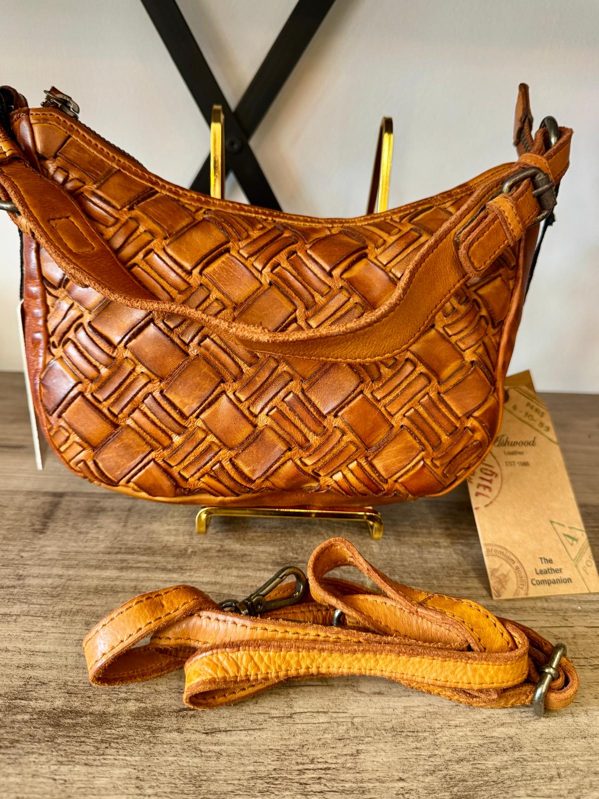 Brown woven leather handbag on a wooden surface with a blurred background