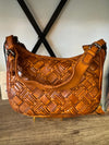 Brown woven handbag on a wooden surface with a white wall background