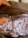 Hand opening a brown leather handbag with crumpled gray paper inside.