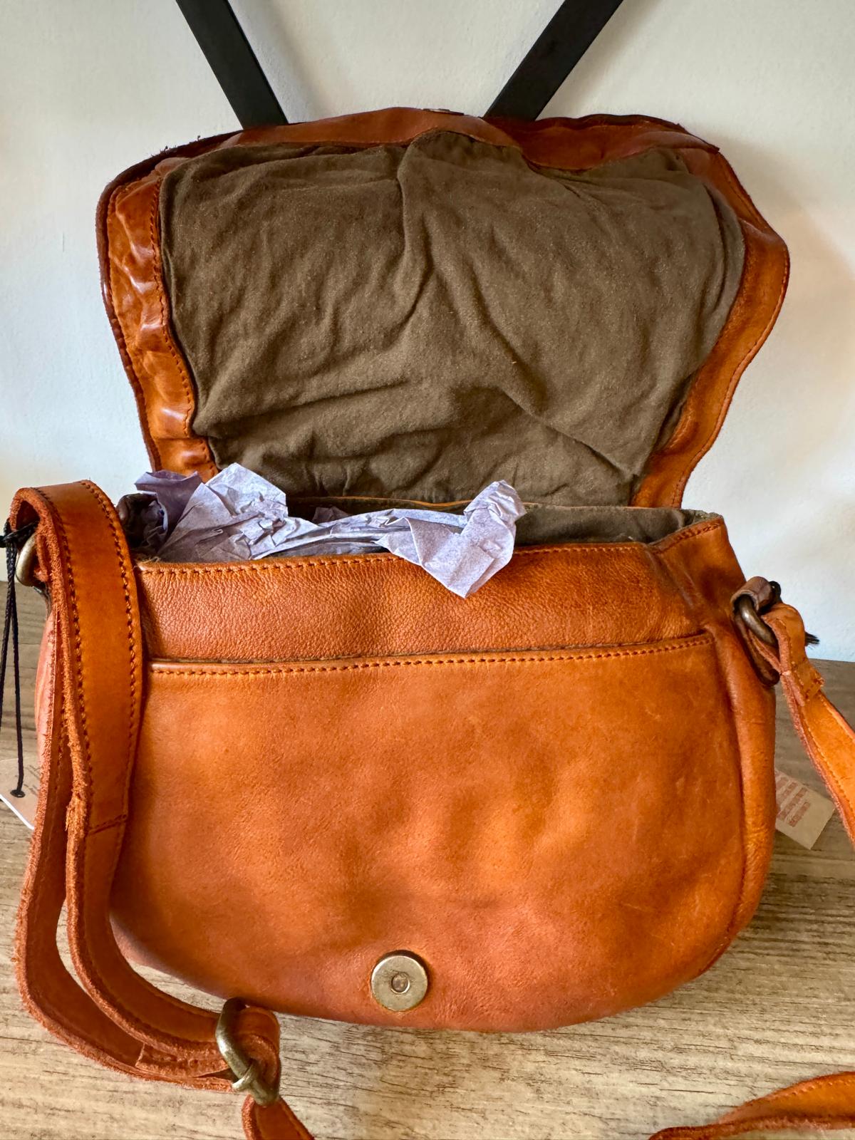 Brown leather handbag with a brown interior on a wooden surface.