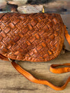 Brown woven leather handbag on a wooden surface with a blurred natural background