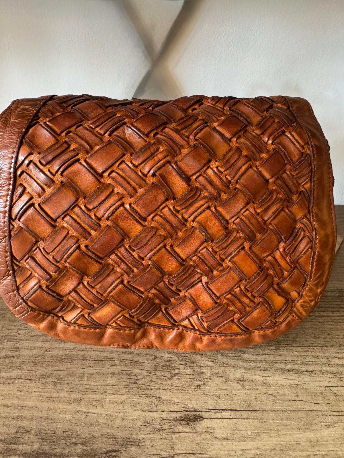 Brown woven leather clutch on a wooden surface