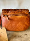 Brown leather handbag with braided top on a wooden surface, featuring a visible brand tag.