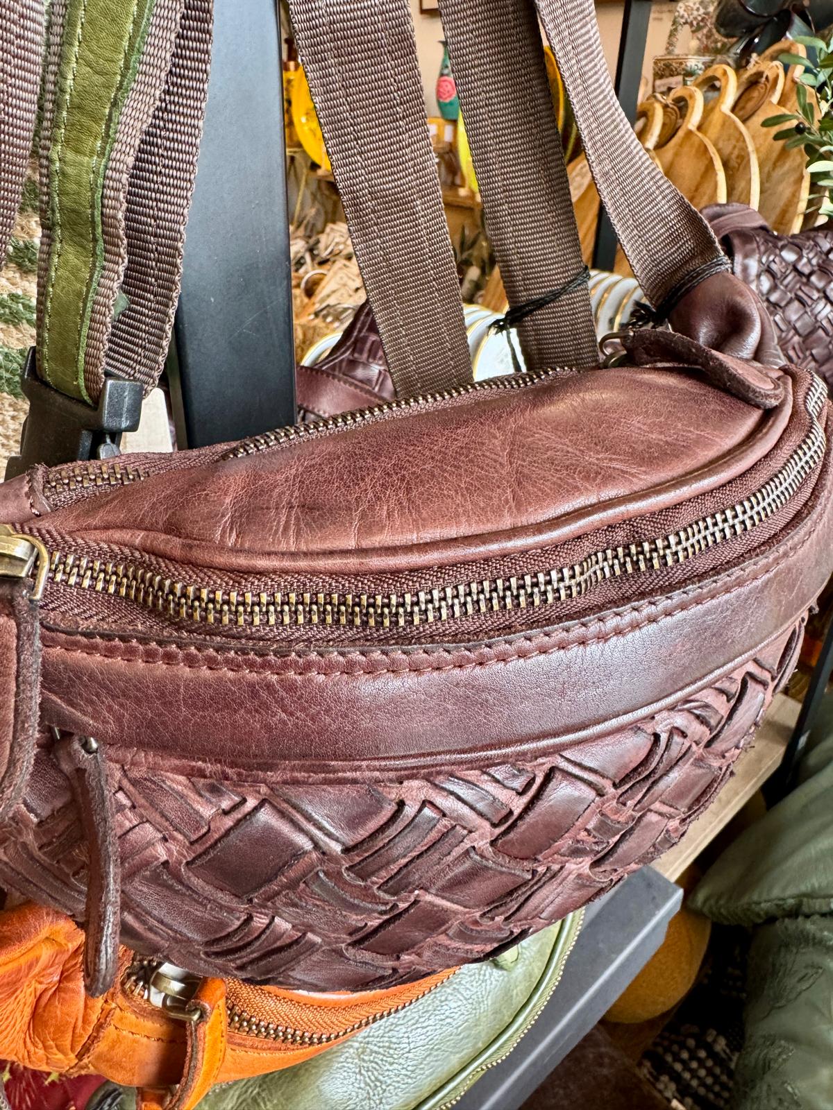 Brown leather waist bag with gold zipper on a blurred background