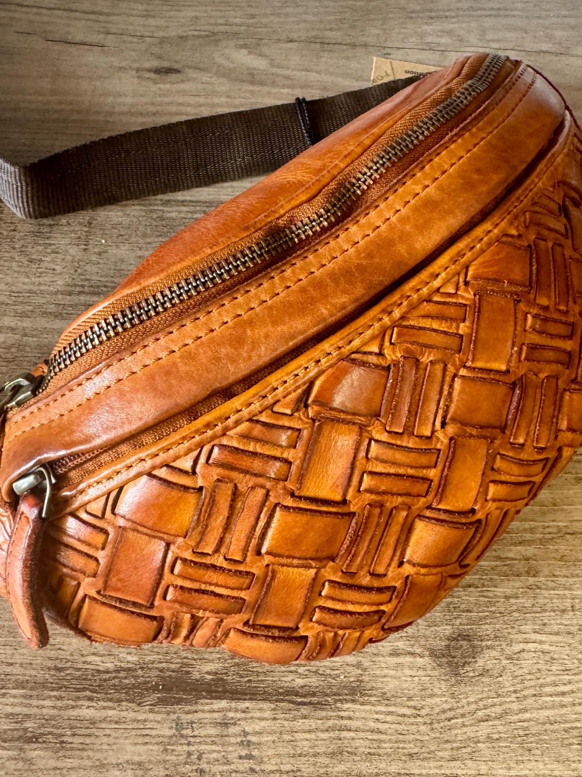 Brown leather waist bag with woven pattern on a wooden surface
