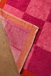Close-up of a pink and orange checkered rug on a concrete floor.