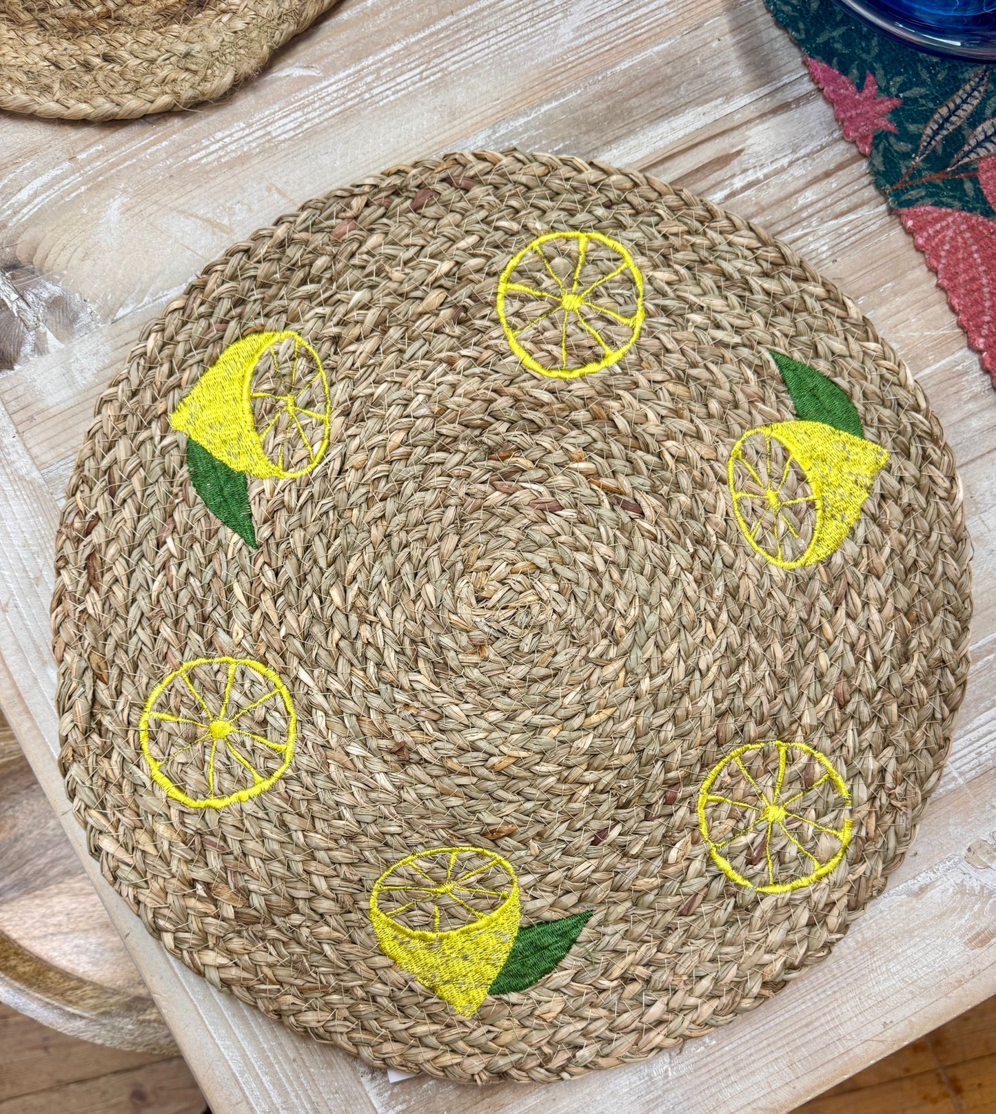 Round woven placemat with embroidered lemon designs on a wooden surface.