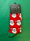 Red sock with Santa Claus pattern on a green background, featuring 'Sock Society' packaging.